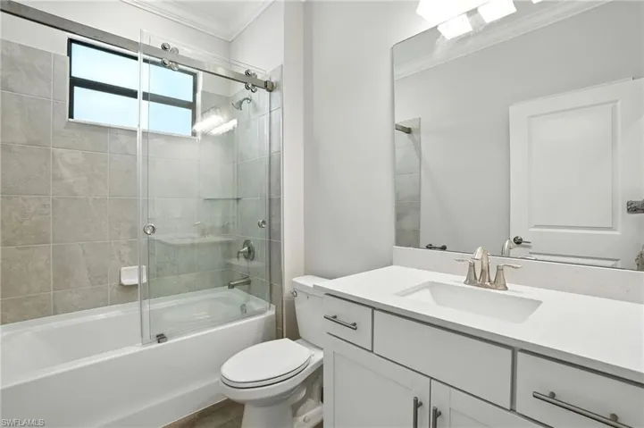 Bathroom with bath / shower combo with glass door, vanity, and ornamental molding