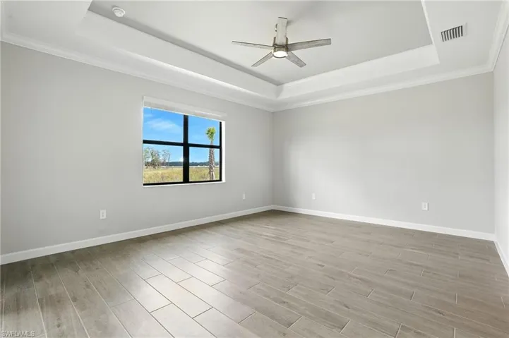 Unfurnished room featuring a raised ceiling, crown molding, light wood-style flooring, and ceiling fan