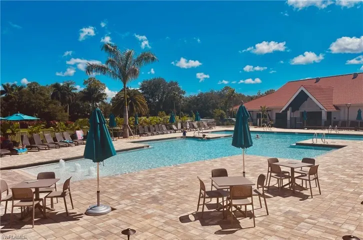 Expansive paver pool deck with multiple swimming pools, water features, and a clubhouse with a terracotta tile roof