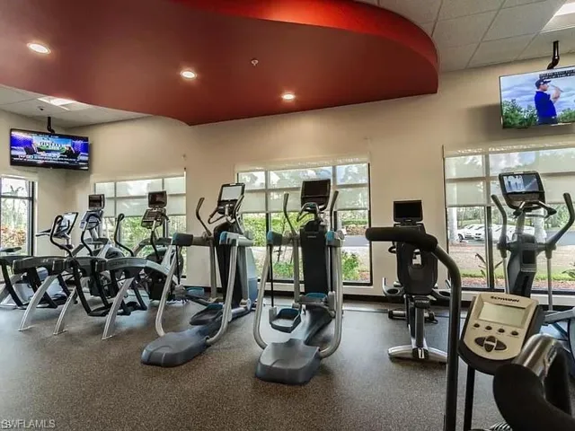 Fitness center with multiple exercise machines, large windows, recessed ceiling lighting, and wall-mounted televisions