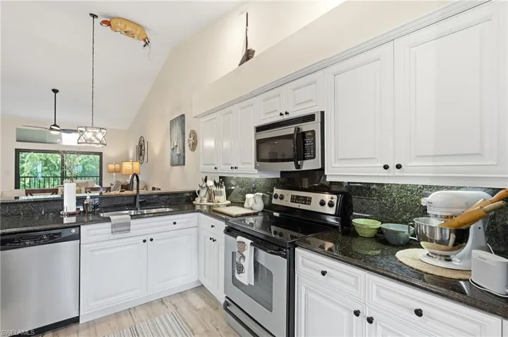 Kitchen featuring white cabinetry, dark stone countertops, stainless steel appliances, and wood-finish flooring