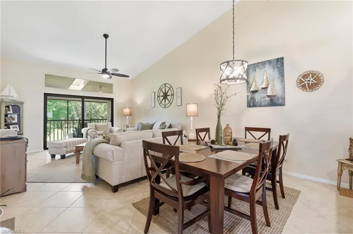 Vaulted ceiling with skylight, tile flooring, ceiling fan, and sliding glass doors to the exterior