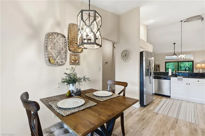 Open-concept kitchen and dining area featuring wood-finish flooring, white cabinetry, dark countertops, and stainless steel appliances