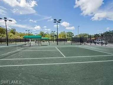 Tennis court featuring a hard surface, perimeter fencing, and overhead lighting