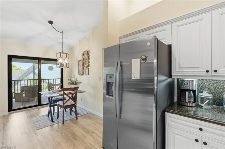 Stainless steel French door refrigerator, white cabinetry with dark hardware, stone countertops, wood-finish flooring, and sliding glass doors leading to a balcony