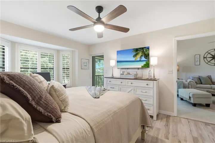 Recessed bay window with plantation shutters, wood-finish flooring, ceiling fan with integrated lighting, built-in white dresser with dark countertop, and direct access to an outdoor area