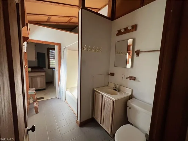 Full bathroom with vanity, vaulted ceiling, tile patterned flooring, toilet, and shower / bath combo with shower curtain
