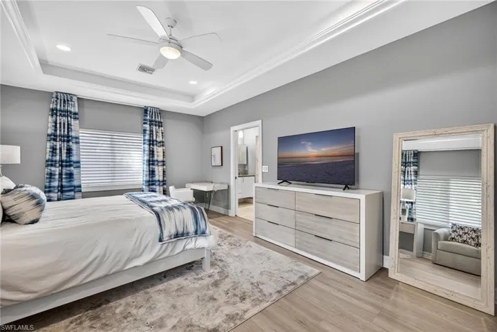 Bedroom with light wood-type flooring, ceiling fan, recessed lighting, connected bathroom, and a tray ceiling