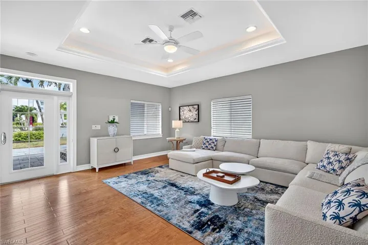 Living area with healthy amount of natural light, wood finished floors, a ceiling fan, a tray ceiling, and recessed lighting