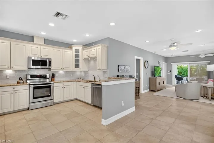 Kitchen featuring appliances with stainless steel finishes, ceiling fan, glass insert cabinets, light tile patterned flooring, and light stone countertops