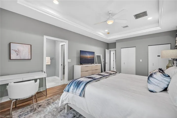 Bedroom featuring multiple closets, a raised ceiling, wood finished floors, recessed lighting, and ceiling fan