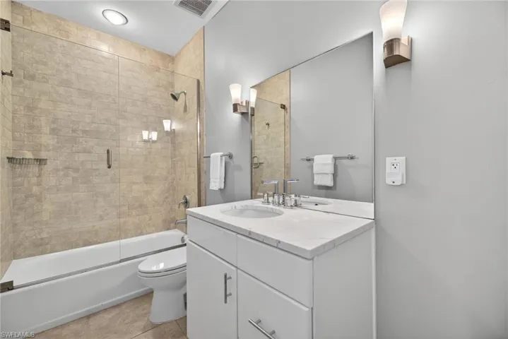 Full bath with vanity, bath / shower combo with glass door, and light tile patterned floors
