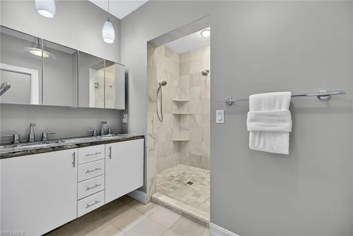 Full bath with double vanity, a tile shower, and light tile patterned flooring