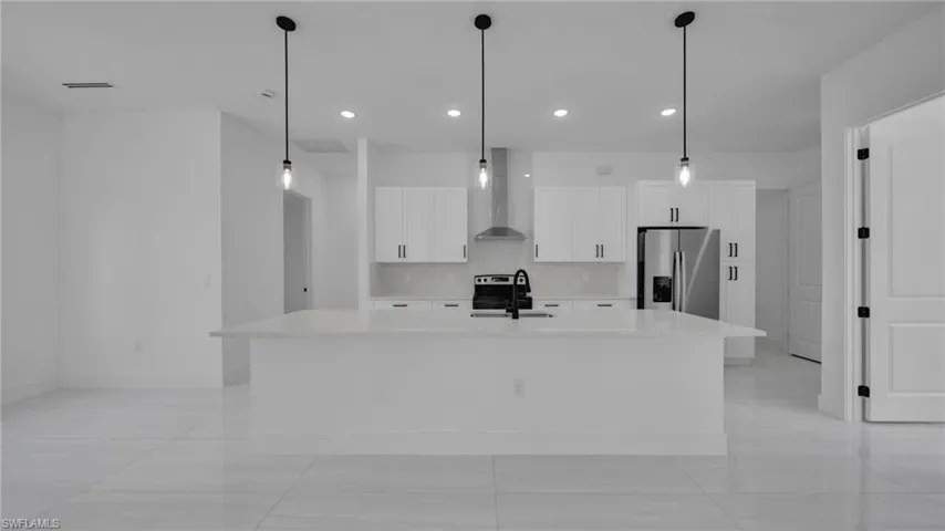 Kitchen featuring hanging light fixtures, wall chimney exhaust hood, appliances with stainless steel finishes, white cabinetry, and light stone countertops