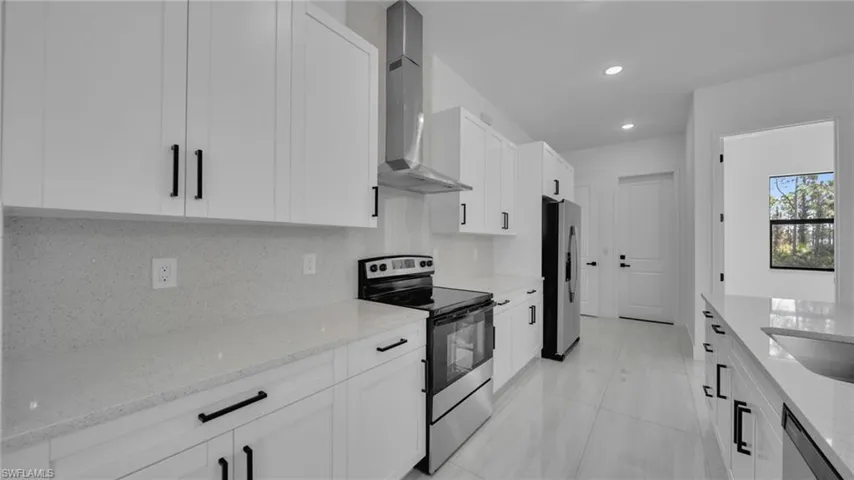 Kitchen with stainless steel appliances, wall chimney exhaust hood, light stone counters, white cabinetry, and backsplash