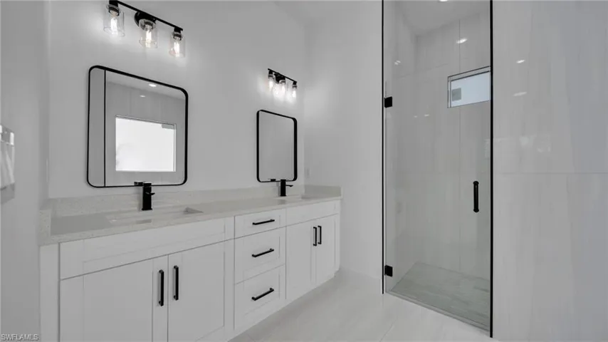 Bathroom with double vanity, a shower stall, and light tile patterned floors