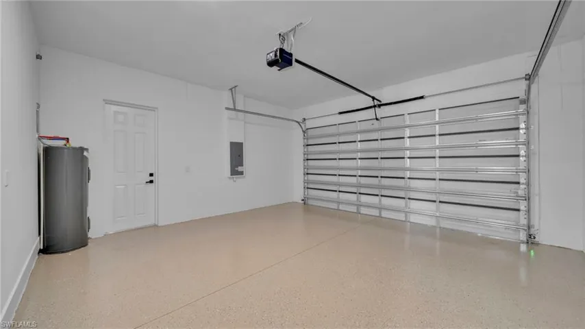 Garage with electric water heater, electric panel, and a garage door opener