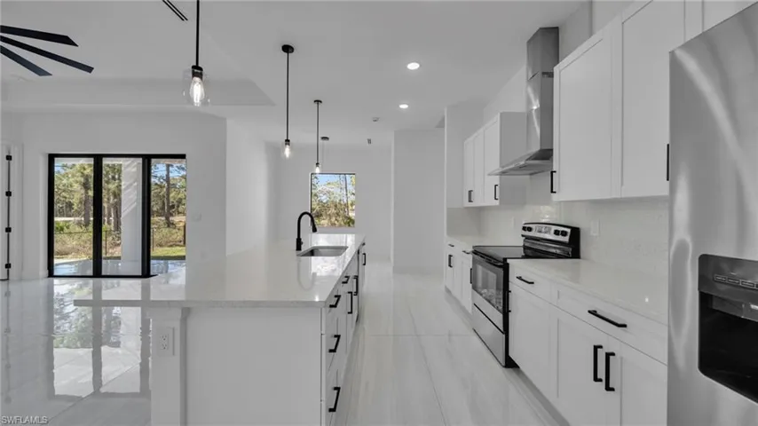 Kitchen featuring appliances with stainless steel finishes, white cabinets, hanging light fixtures, wall chimney range hood, and recessed lighting