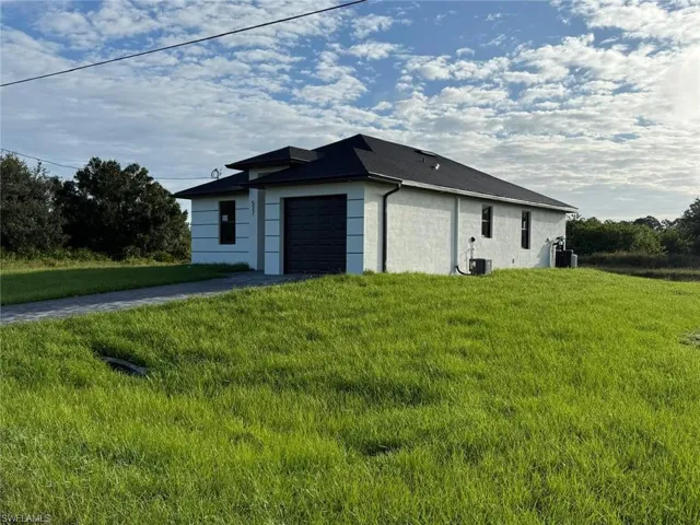 View of side of property featuring a lawn, driveway, stucco siding, and an attached garage