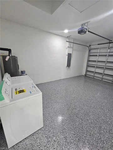 Garage with electric water heater, a textured wall, electric panel, and a garage door opener