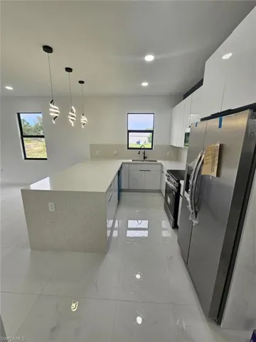 Kitchen featuring stainless steel appliances, a peninsula, light stone counters, decorative light fixtures, and modern cabinets