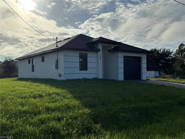 View of side of property with a garage, a lawn, stucco siding, and asphalt driveway