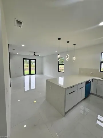 Kitchen with light marble finish flooring, open floor plan, light stone counters, hanging light fixtures, and ceiling fan