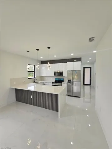 Kitchen with a peninsula, stainless steel appliances, white cabinetry, light stone countertops, and hanging light fixtures