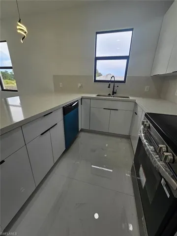 Kitchen with modern cabinets, stainless steel stove, light stone counters, and white cabinets