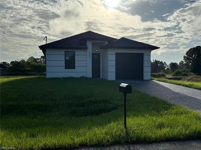 View of front of home with decorative driveway, a front lawn, and a garage