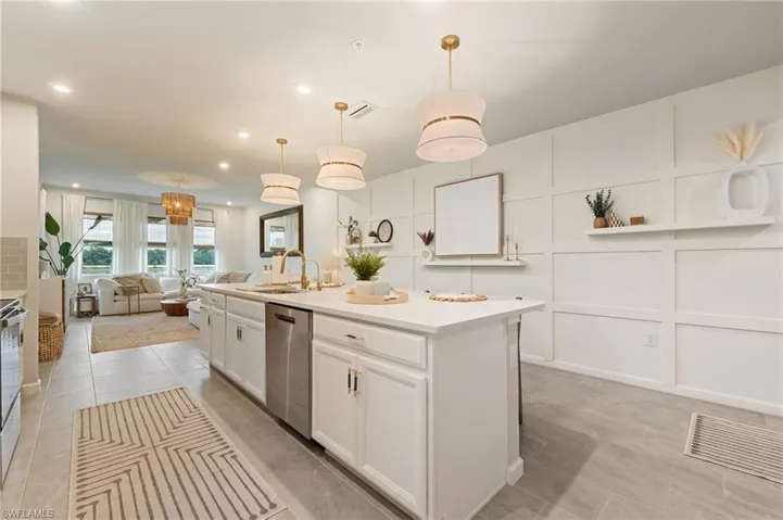 Kitchen with a center island with sink, a decorative wall, open floor plan, pendant lighting, and white cabinetry
