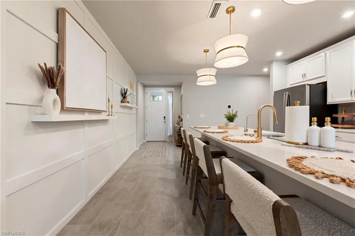 Kitchen with hanging light fixtures, white cabinets, freestanding refrigerator, a decorative wall, and recessed lighting
