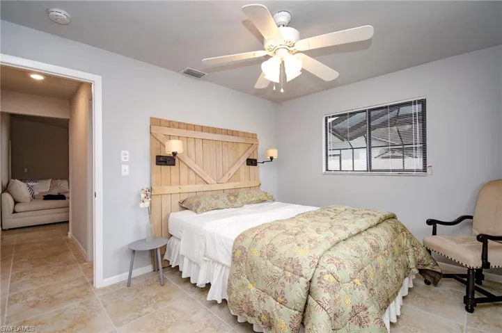 Bedroom featuring a wood-panel accent wall with integrated sconces, tiled flooring, and a ceiling fan with integrated lighting