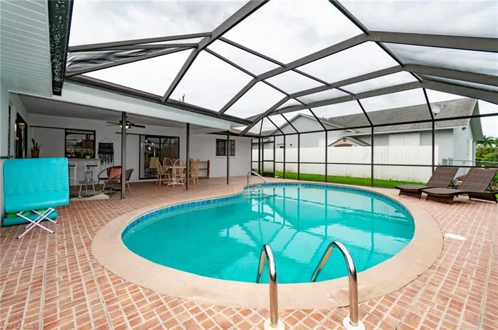 Screened-in pool area featuring a free-form pool, brick-patterned patio, and an extended covered lanai