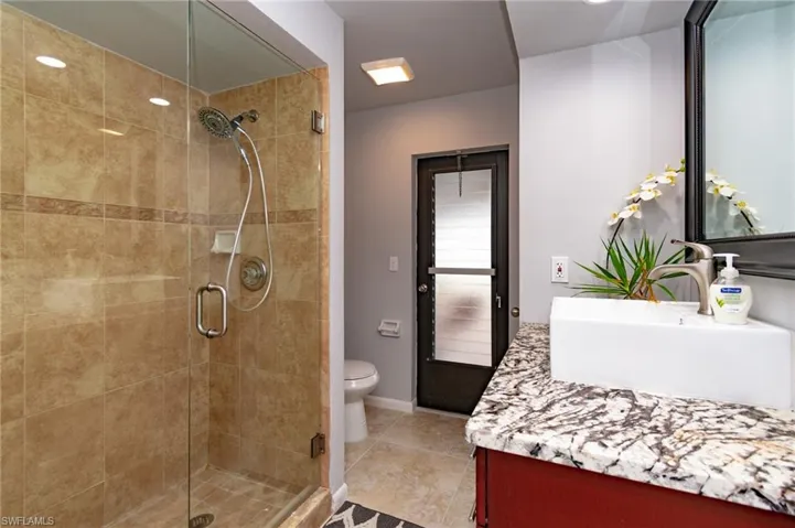 Bathroom featuring a glass-enclosed shower with tile surround, a vessel sink, a granite-patterned countertop, and a dark wood-paneled door