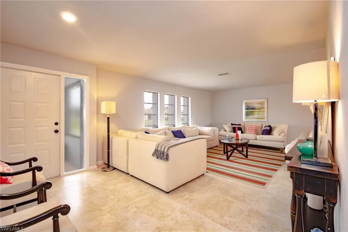 Spacious interior with tile flooring throughout, featuring a paneled entry door with frosted sidelight, recessed lighting, and multiple windows