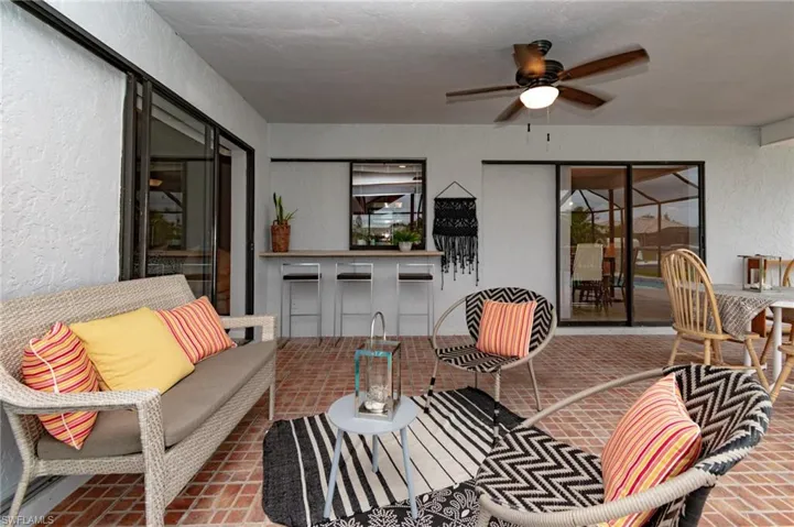 Covered patio featuring brick-laid flooring, a built-in bar with barstools, a ceiling fan, and multiple sliding glass doors