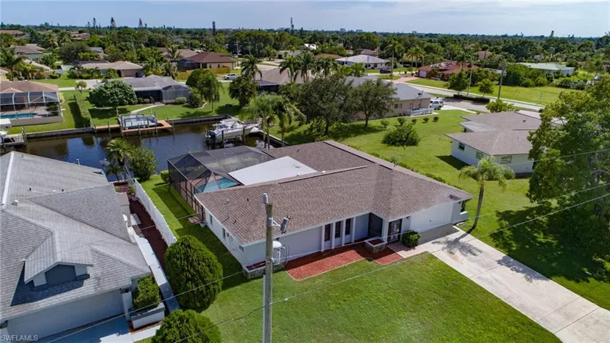 Waterfront residence featuring a screened pool enclosure, private dock, mature landscaping, and an attached garage
