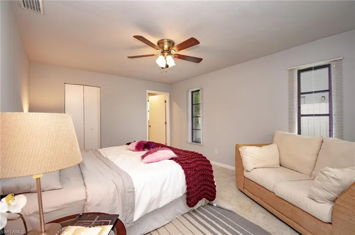 Neutral-toned bedroom featuring a ceiling fan with light fixture, carpeted flooring, and two windows