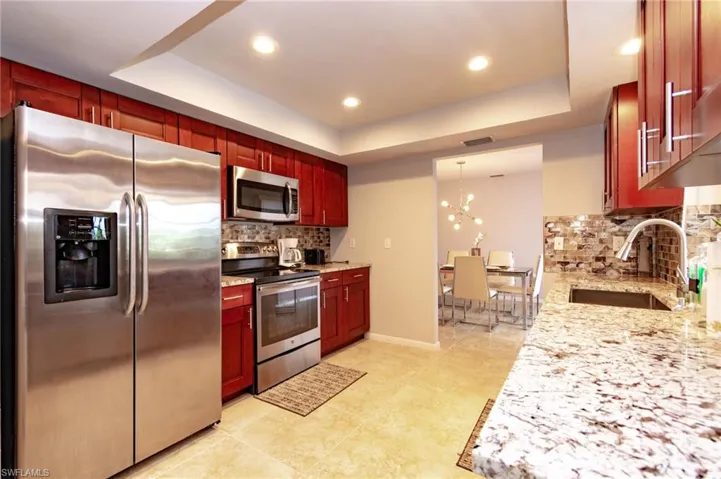 Kitchen featuring cherry wood-finish cabinetry, stainless steel appliances, speckled stone countertops, and a mosaic tile backsplash