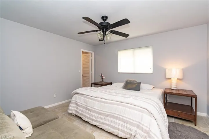 Room featuring light neutral wall paint, tile flooring, a ceiling fan with integrated lighting, a window with blinds, and a louvered door