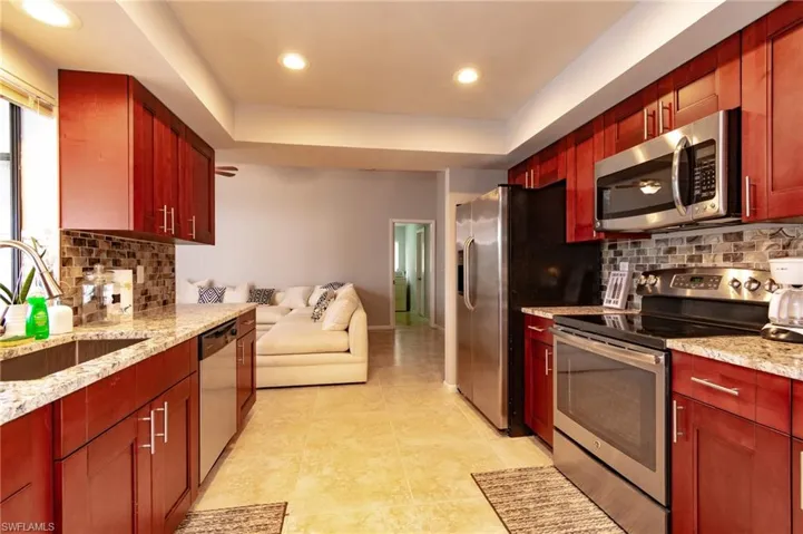Galley kitchen featuring cherry-finish cabinetry, granite-style countertops, mosaic tile backsplash, and stainless steel appliances including a built-in microwave and full-size refrigerator