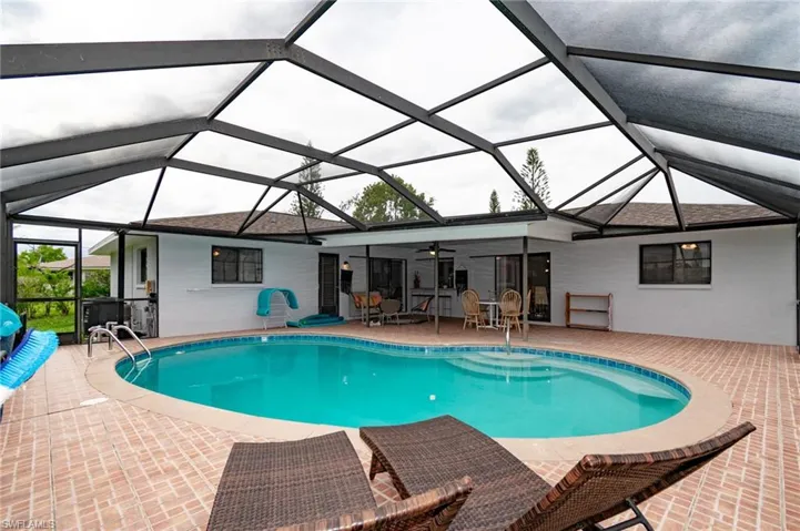 Screened outdoor living area featuring a kidney-shaped pool with integrated steps, surrounded by brick-finish pavers