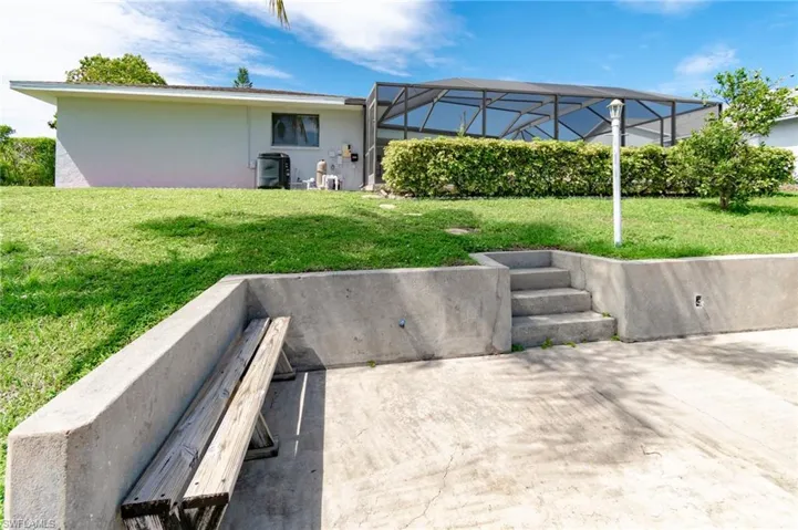 Tiered backyard featuring a concrete patio with built-in steps, a screened enclosure, and a manicured lawn
