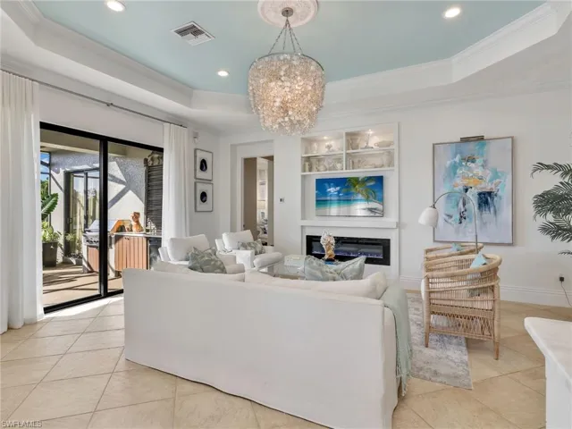 Living room featuring a tray ceiling, a glass covered fireplace, crown molding, a chandelier, and recessed lighting