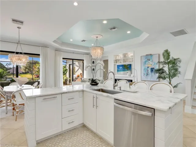 Kitchen with a chandelier, stainless steel dishwasher, light stone counters, white cabinetry, and a tray ceiling