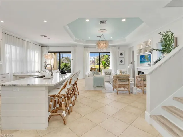 Kitchen with light stone counters, a tray ceiling, a chandelier, decorative light fixtures, and ornamental molding