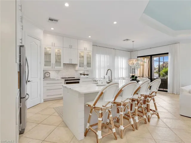 Kitchen featuring glass insert cabinets, decorative light fixtures, backsplash, a breakfast bar area, and white cabinets
