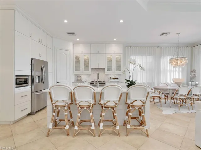 Kitchen with glass insert cabinets, decorative backsplash, ornamental molding, white cabinets, and a kitchen breakfast bar