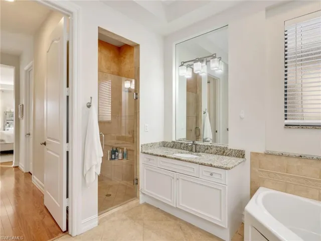 Ensuite bathroom with vanity, a stall shower, a bath, light tile patterned floors, and tile walls